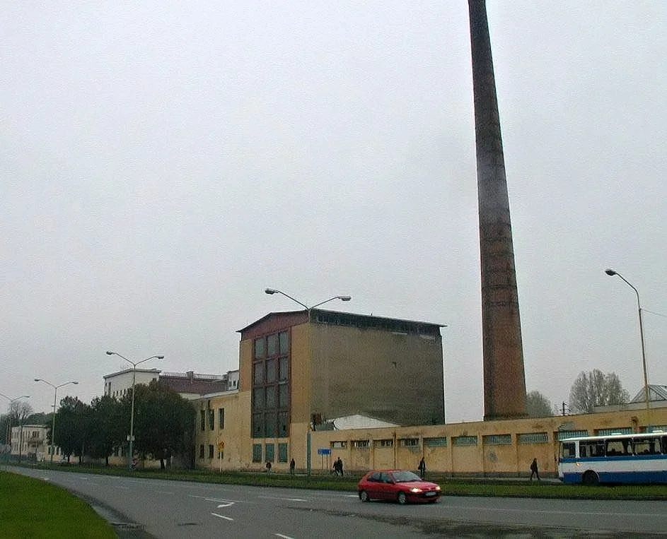 Pivovar krátko pred zánikom. Vysoký tehlový komín a žltá hlavná budova v hmlistom dni.