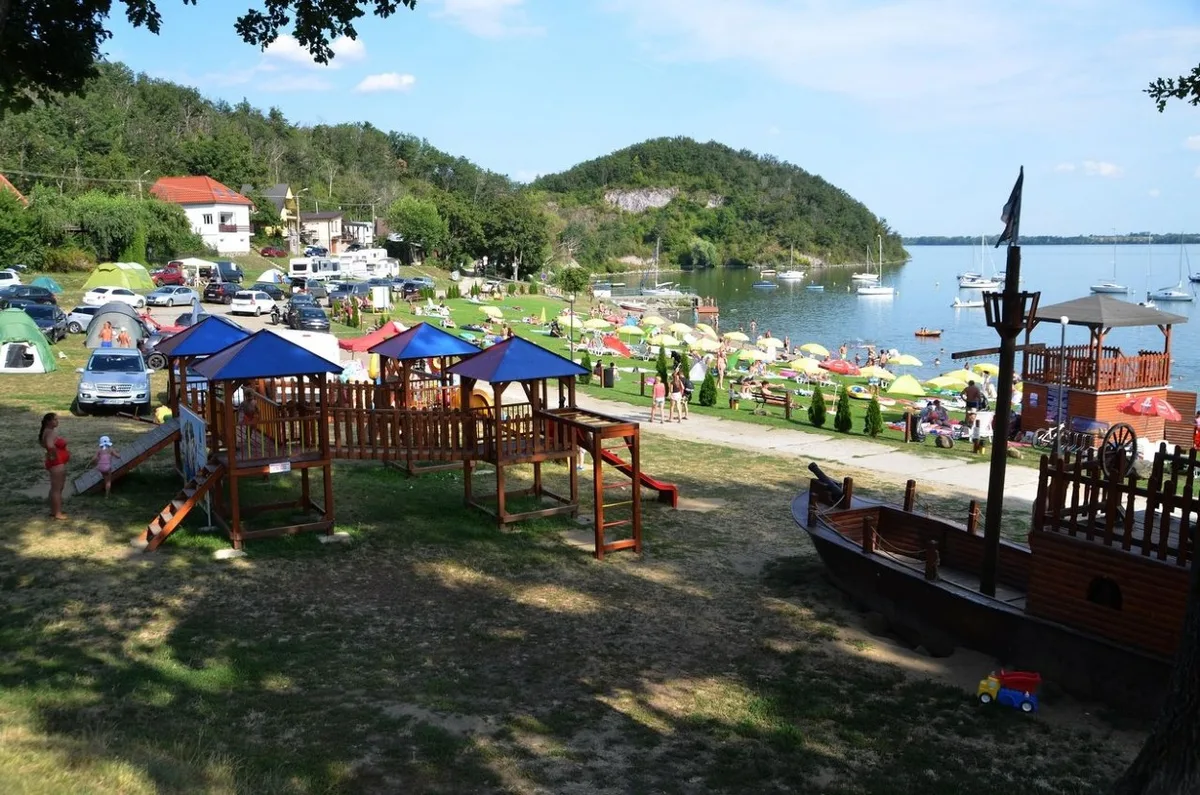Detské ihrisko a drevená pirátska loď nad plážou na Hôrke, v pozadí slnečníky, jachty a hladina Zemplínskej šíravy.